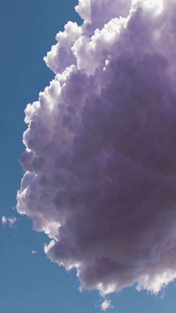 A dramatic low-angle shot of a towering, fluffy cloud against a clear blue sky, resembling a video