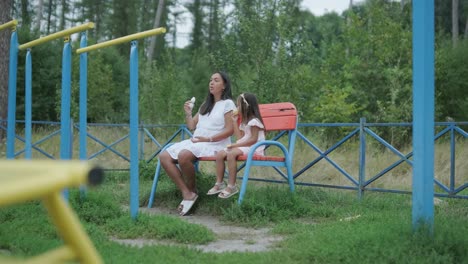 a pregnant mother and her young daughter enjoy playful time together at a playground in the park, surrounded by trees and greenery