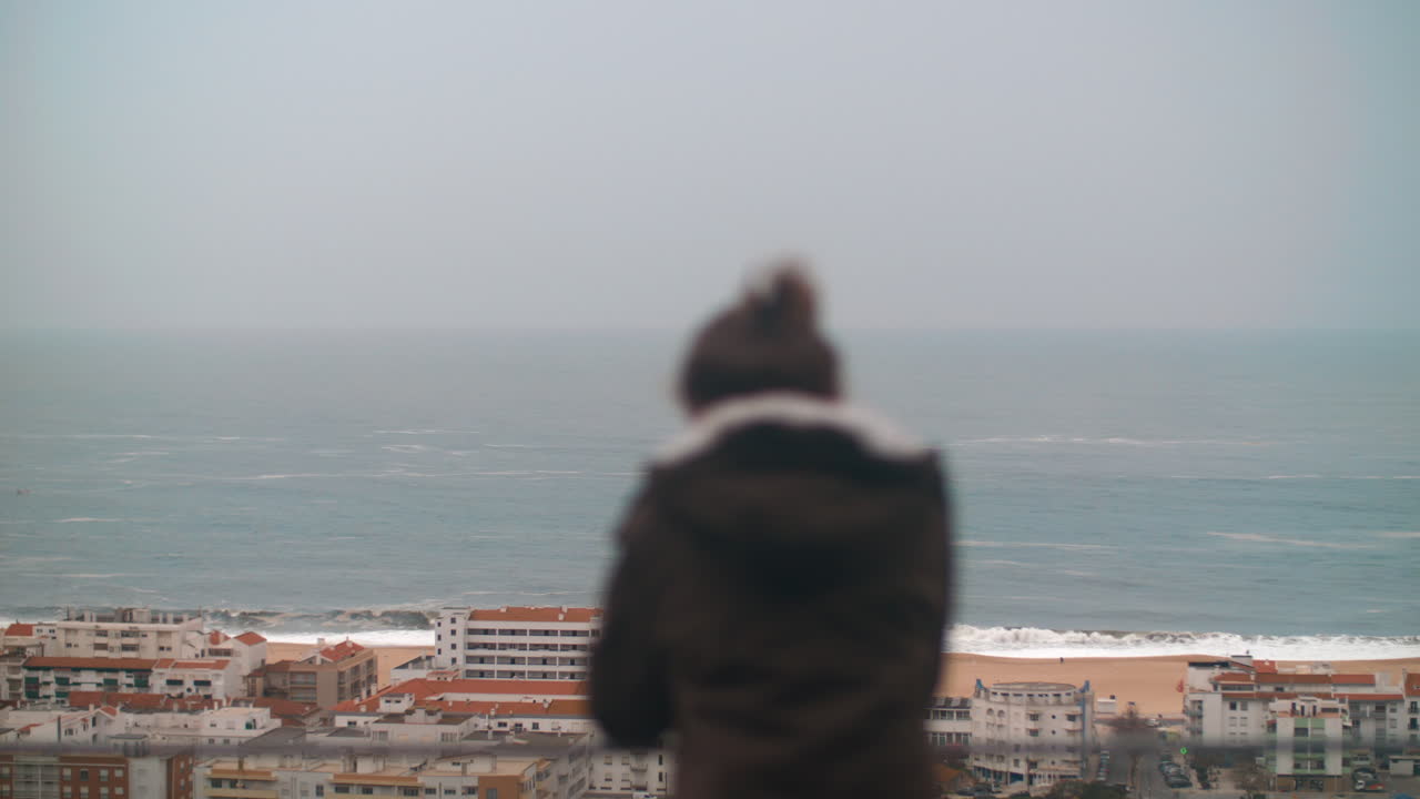 Lonely child looking at the ocean and coastal resort town of Nazare Portugal