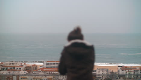 Lonely-child-looking-at-the-ocean-and-coastal-resort-town-of-Nazare-Portugal