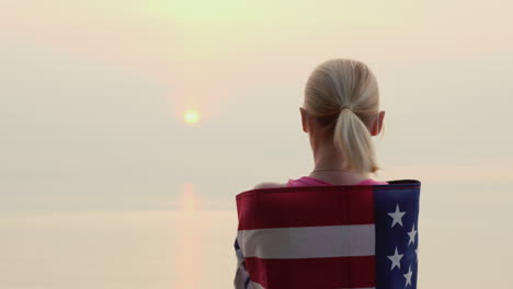 a woman with the flag of america on her shoulders looks at the sunrise over the sea