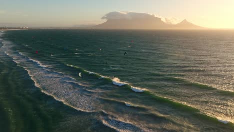 Sunset-view-of-a-kitesurf-beach-near-Cape-Town-with-a-kitesurfer-jumping,-slow-motion-aerial-shot