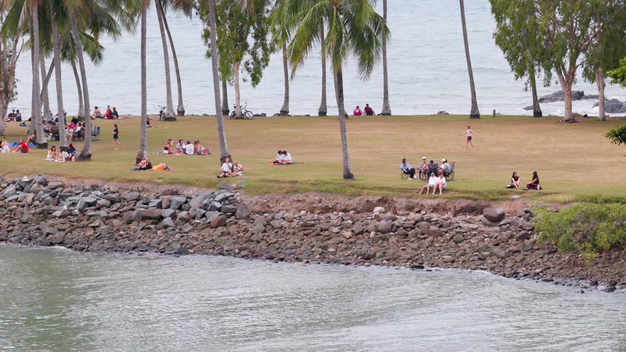 Aerial view of people enjoying a riverside picnic under palm trees in Port Douglas, Queensland. Calm, serene atmosphere with gentle camera movement