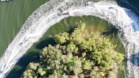 jet skis create dynamic patterns around a lush, green island from an aerial perspective.