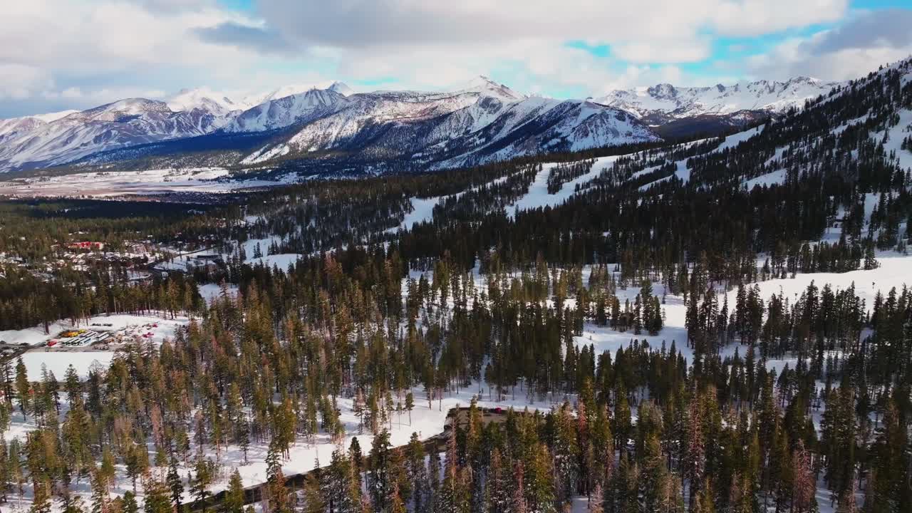 Main lodge Mammoth Mountain ski resort car parking lot California aerial drone chairlifts Inyo National Forest skiing snowboarding winter sunny blue sky ski trail runs afternoon forward motion