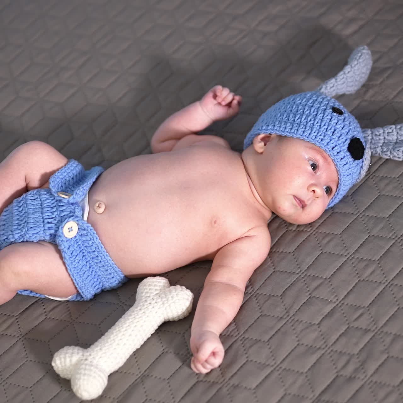 Adorable baby in costume of a puppy on the bed. Kid lying and moving his arms and legs quickly. Cute child yawning