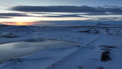 Drohnen-Doley-Aufnahme-Einer-Langen-Pipeline,-Die-Nach-Sonnenuntergang-Die-Weiße-Winterlandschaft-Islands-Durchquert