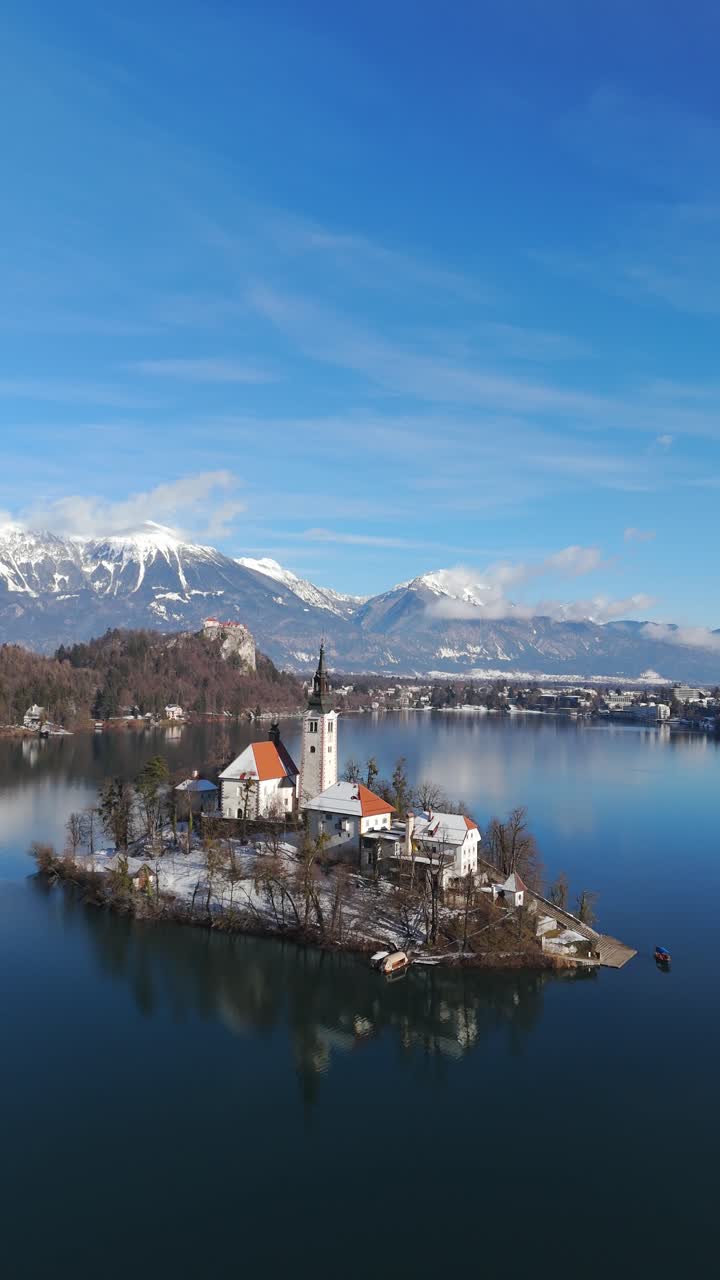 Bled Gölü, Slovenya, kış, dikey drone yörüngesi, ada kilisesi, kale, alp dağları, sakin su ve kar manzarası