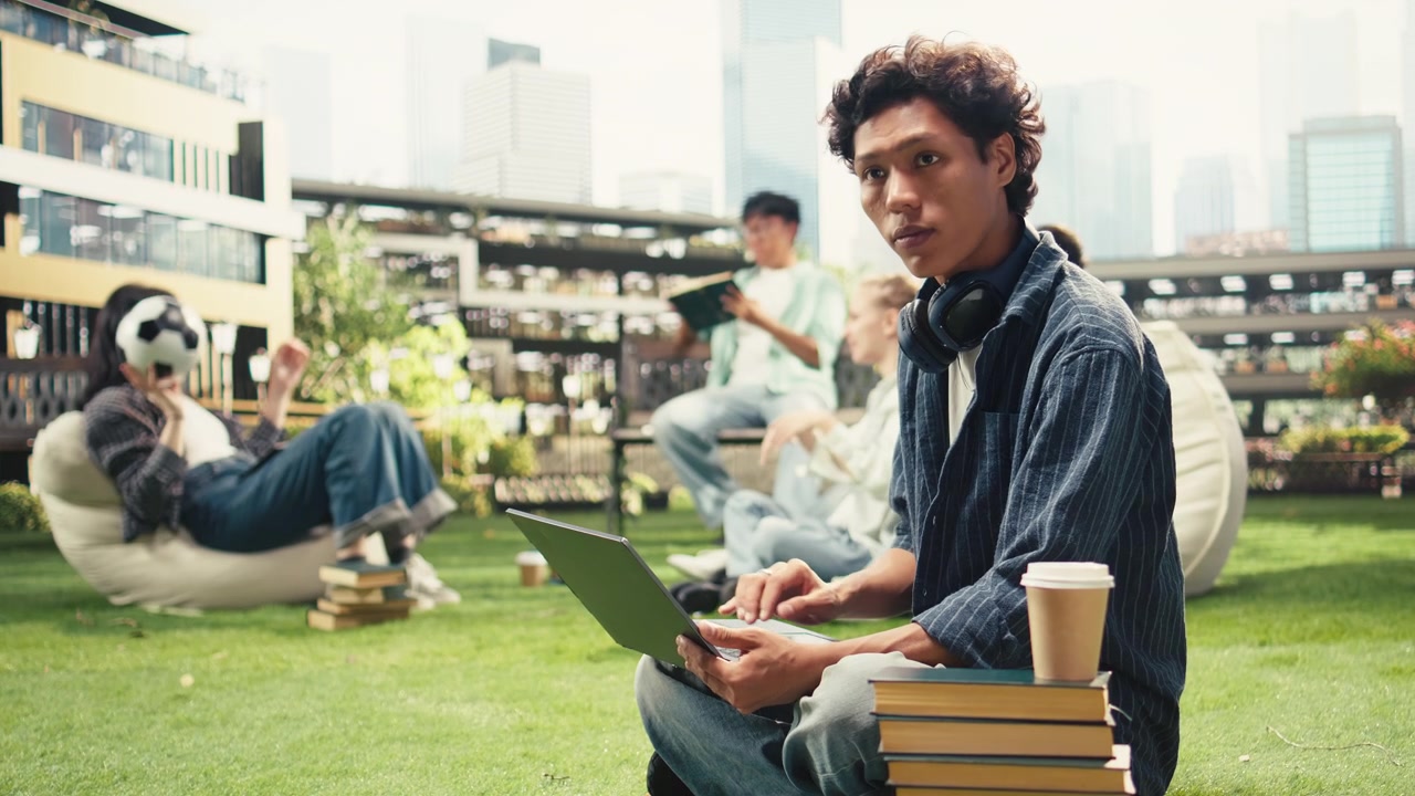 Portrait of smiling international student working on laptop while relaxing on grass