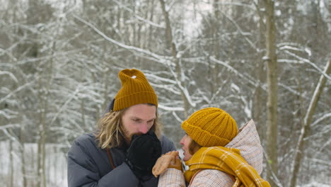 hombre y mujer calentándose las manos en el bosque nevado