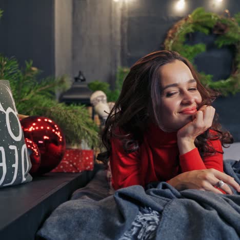 happy woman on christmas decorations background. young woman in red sweater is lying on the bed with pleasure in winter holidays. happy winter holidays concept.