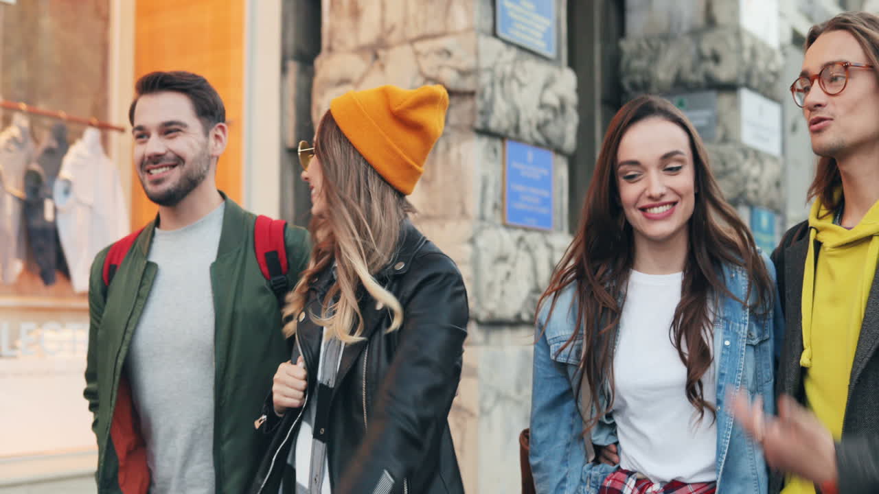 retrato de un joven grupo de amigos caucásicos caminando por la calle mientras hablan y se ríen en la ciudad