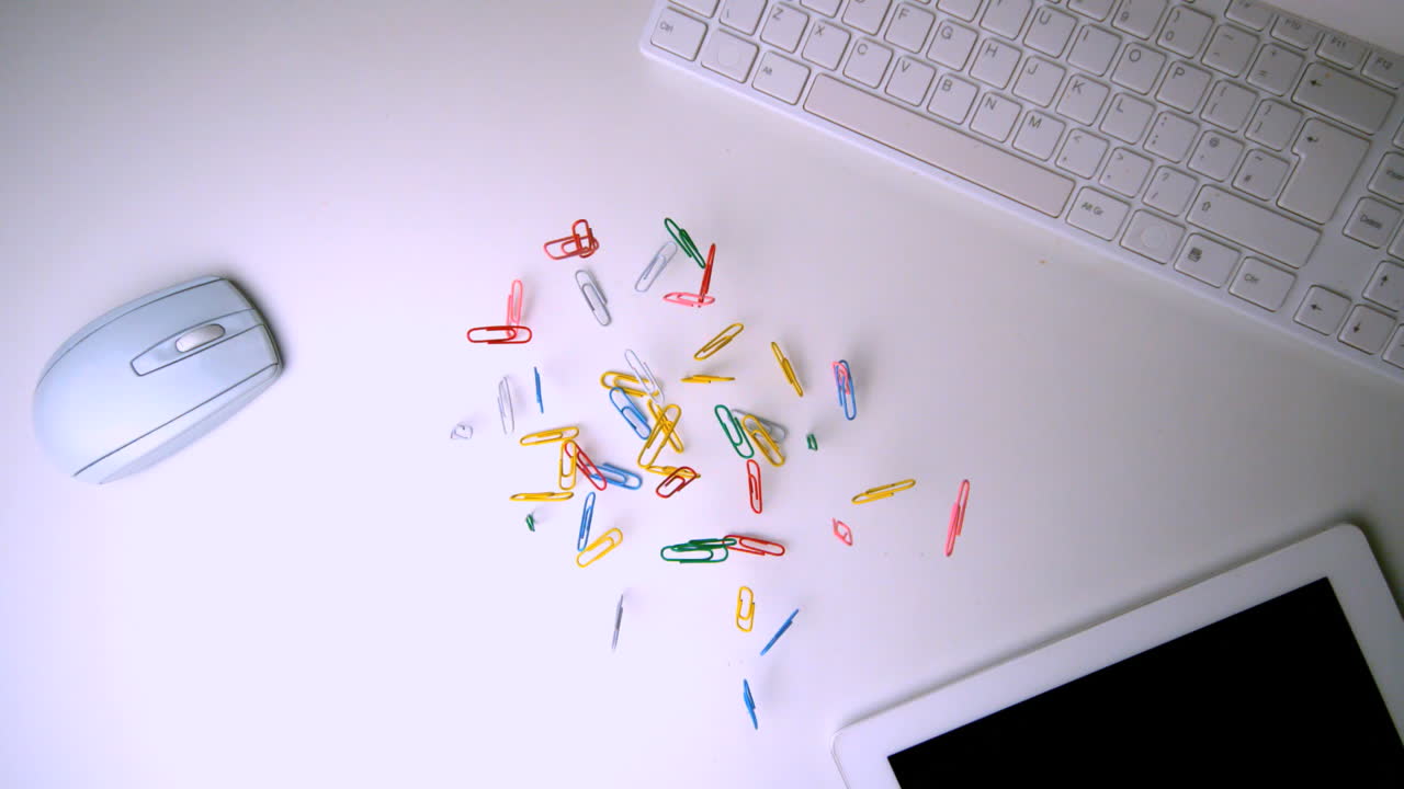 Colourful paperclips falling on office desk