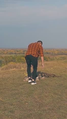 guy in orange shirt with hangover goes out of blue tent and walks to bonfire in early morning slow motion backside view