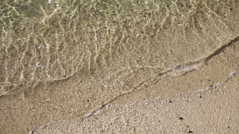 Top-down-slow-motion-shot-of-crystal-clear-waves-crashing-on-a-sandy-beach-in-NewZealand