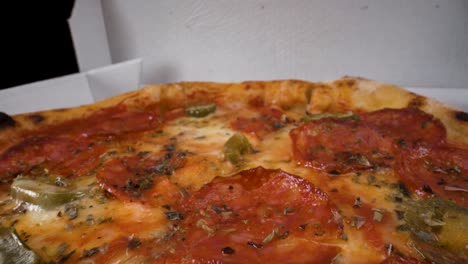 Vista-Macro-En-Movimiento-Inverso-De-La-Pizza-Pepperoni-Jalapeño-Cerrada-En-Una-Caja-De-Cartón-Para-Llevar-Con-Fondo-Negro,-Cocina-Italiana-De-4k