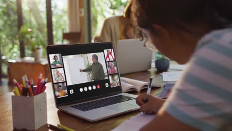 Schoolgirl-using-laptop-for-online-lesson-at-home,-with-diverse-teacher-and-class-on-screen