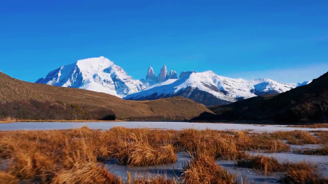 Une vue aérienne cinématographique à couper le souffle, capturant les emblématiques aiguilles de granit enneigées de Torres del Paine s'élevant au-dessus d'un lac alpin parsemé de glace