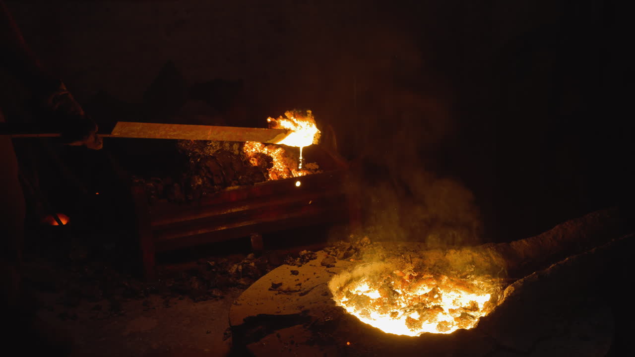 어두운 주조장에서 일하는 노동자가 긴 막대기로 금속을 녹이는 경향이 있습니다.