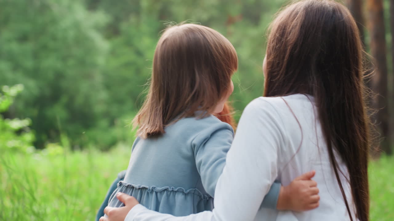 푸른 숲과 밝은 여름 햇살이 내리쬐는 피크닉 장소 옆에서 사랑스러운 엄마가 행복하게 지켜보는 가운데, 형제자매가 서로 따뜻하게 껴안으며 미소짓는 즐거운 야외 가족 풍경