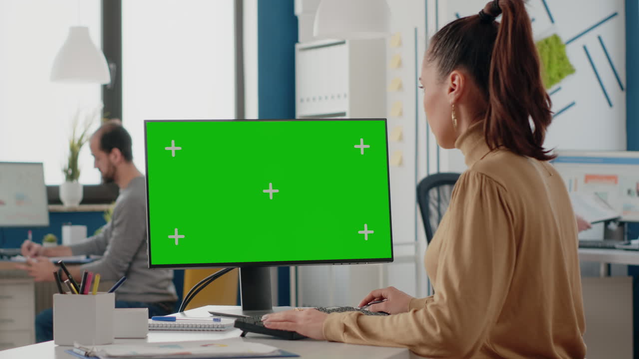 Woman working with isolated green screen on monitor at desk