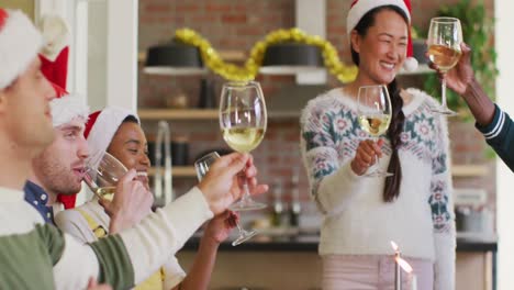 happy group of diverse friends in santa hats celebrating meal, toasting with vine at christmas time