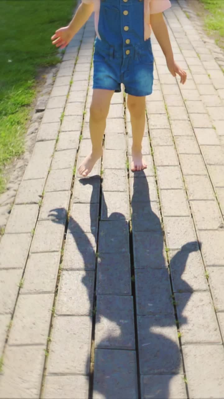 Child walking barefoot on a sunny pathway, casting a playful shadow on the ground