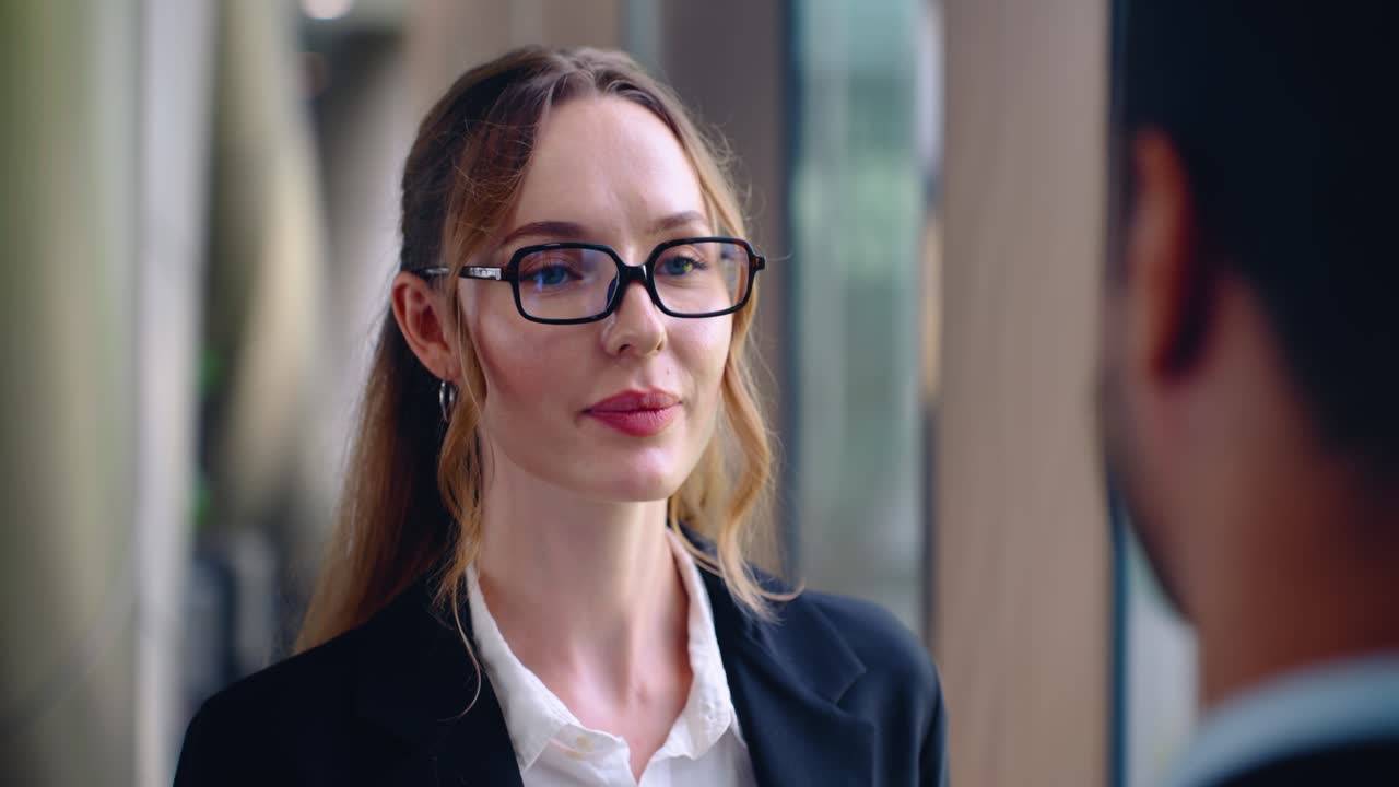 Smiling business woman talking with male colleague during informal hallway office meeting indoors, medium closeup