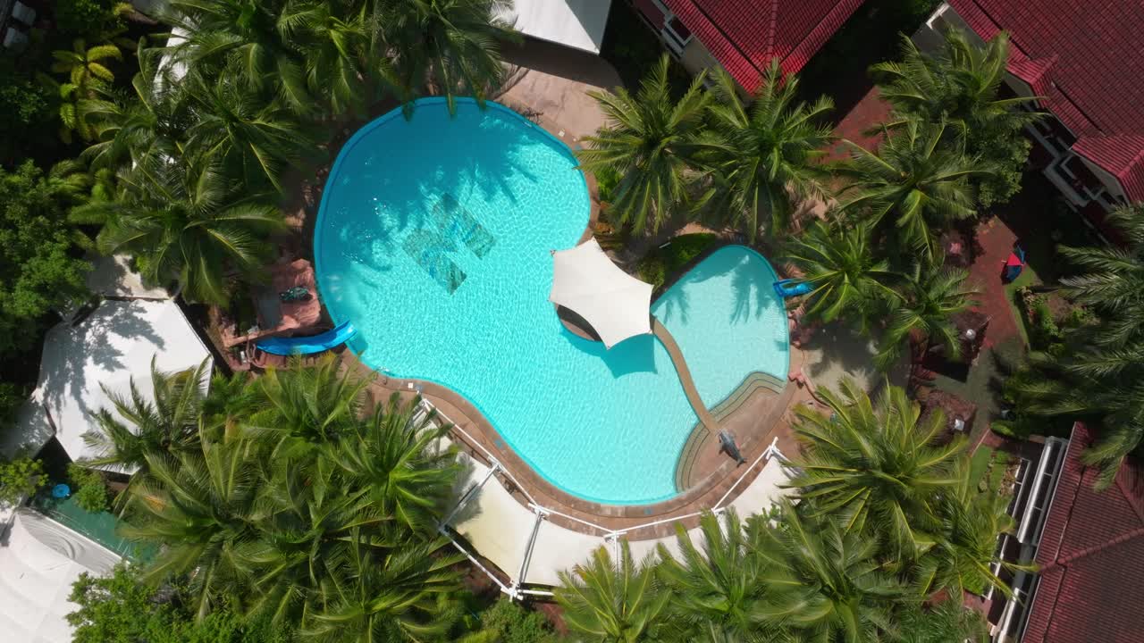 Et filmisk dolly-in droneoptagelse afslører en luksuriøs resortpool, der udvides for at vise dens fredfyldte omgivelser og tropiske atmosfære.