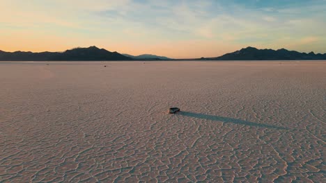 SUV-races-across-barren-Bonneville-Salt-Flats-in-Utah,-aerial-tracking-at-golden-hour