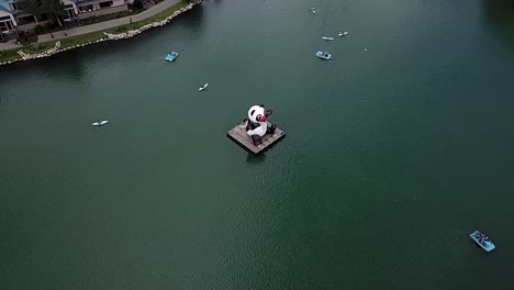 Kayakers-Around-The-Huge-Panda-Figure-In-The-Middle-Of-The-Calm-Lake-In-Washington,-USA---Aerial-Shot