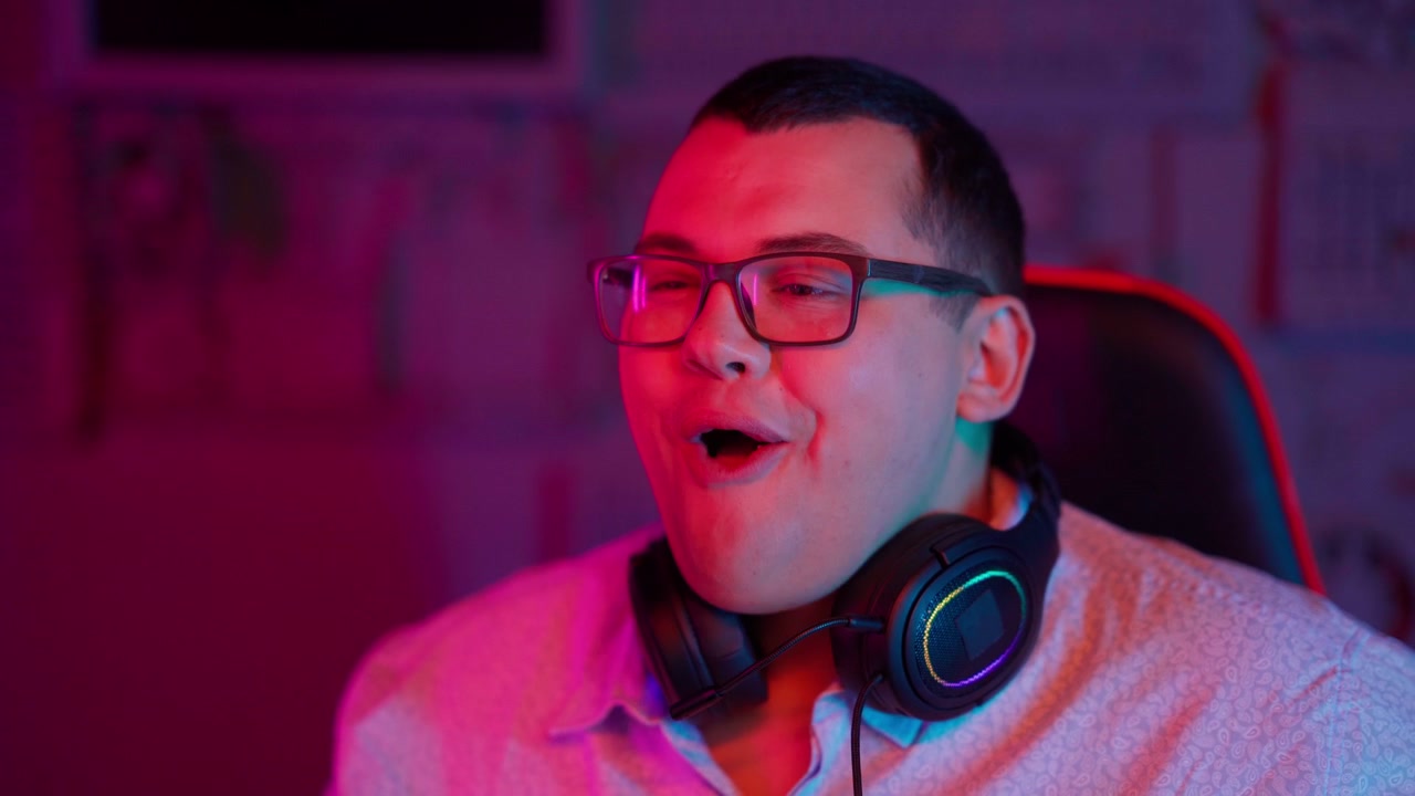Giovane uomo con occhiali e cuffie che mangia popcorn sotto luci al neon.