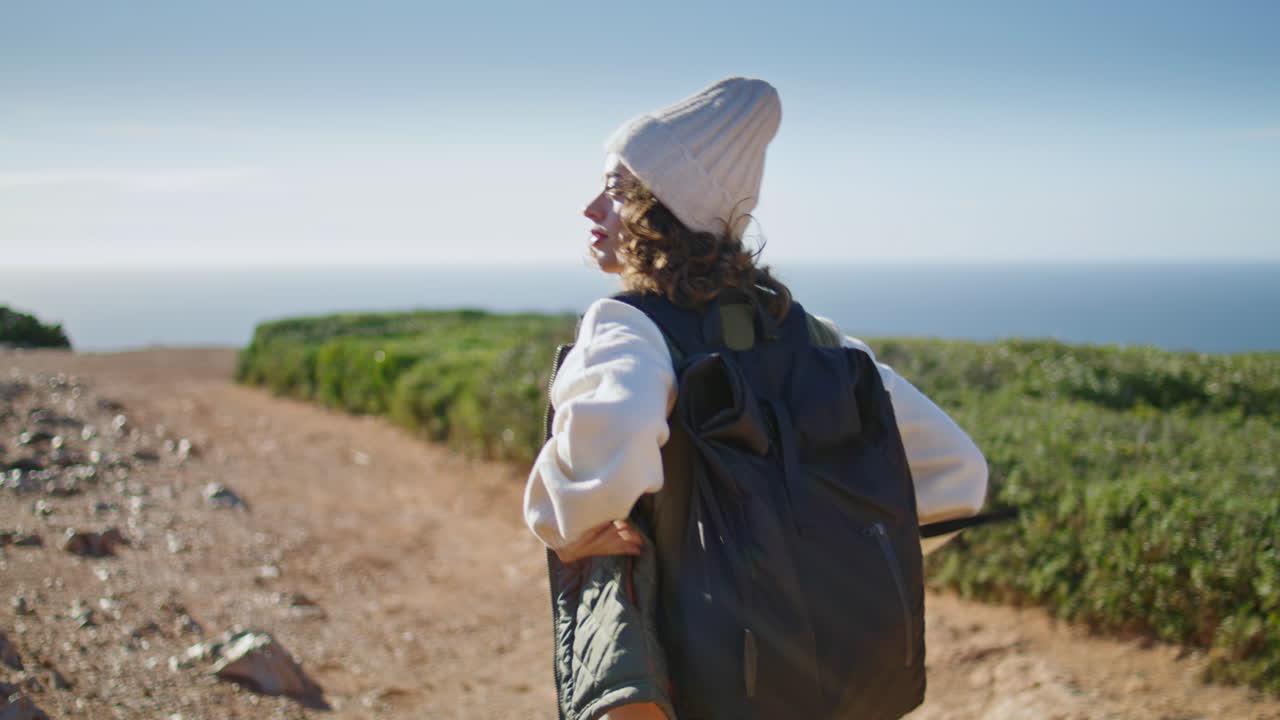 turista caminando por el camino rocoso en la orilla del océano. chica relajada con mochila