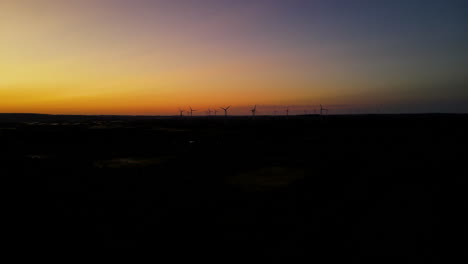 Aerial-shot---flying-towards-the-wind-farm-on-golden-sunset,-wind-turbines-silhouette-far-away-on-background,-Puck,-Pomorskie,-Poland