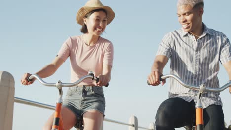 happy biracial couple riding bikes on promenade, in slow motion