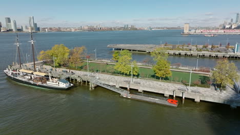 Fliegen-Sie-Um-Das-Sportgelände-Am-Pier-25-Im-Hudson-River-Park.-Historisches-Segelboot,-Das-Am-Liegeplatz-Steht.-Breite-Flusswasseroberfläche-Im-Hintergrund.-Manhattan,-New-York-City,-Vereinigte-Staaten