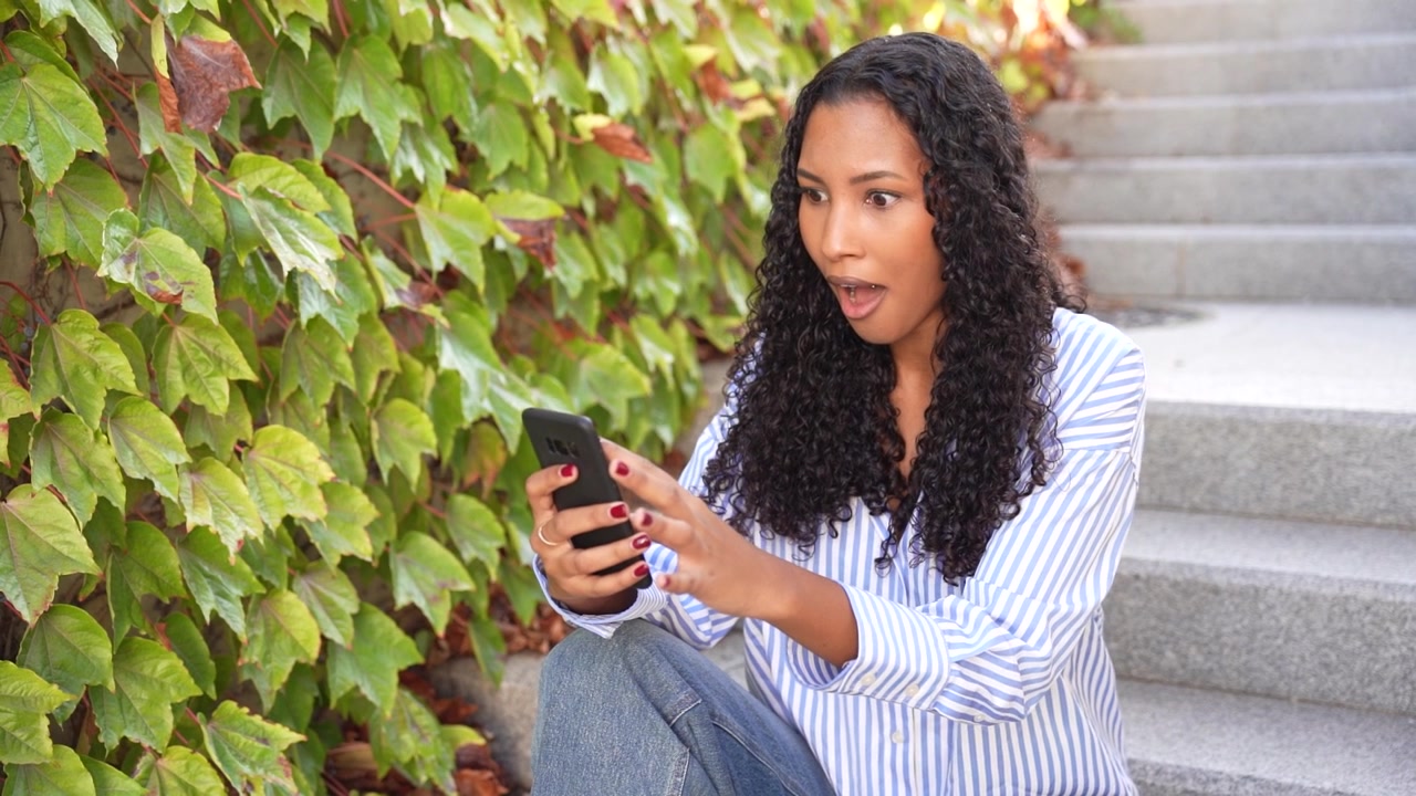 A young woman sits comfortably on steps using her smartphone amidst lush greenery