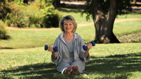 Senior-woman-working-her-muscles-with-dumbbells-on-the-grass