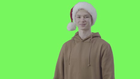 joyful boy in christmas hat crossing hands and smiling at camera. portrait of caucasian teenager posing at green screen background. new year, holidays, joy. chromakey.