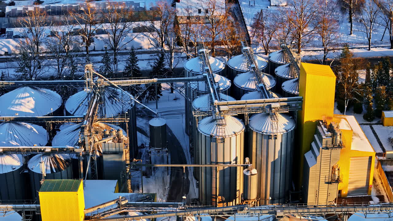 Aerial drone tracking shot moving right past grain silos and industrial facility in winter snow