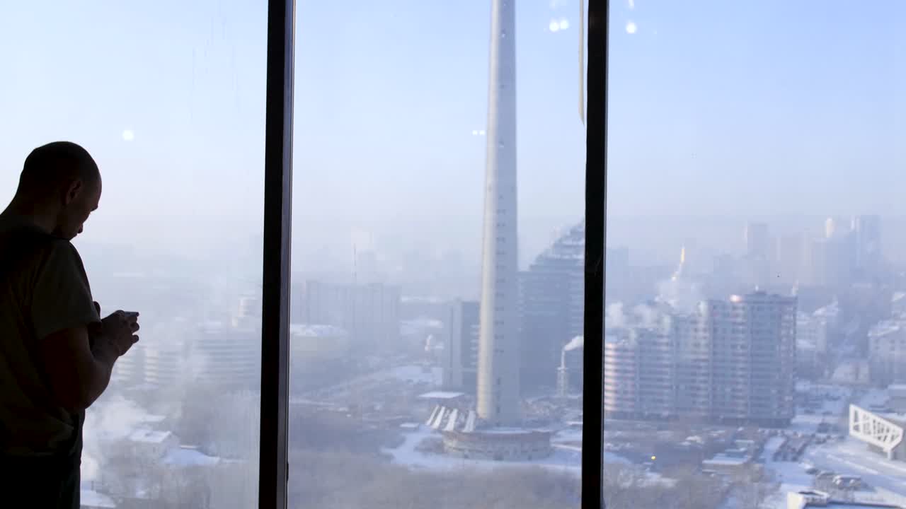 Hombre mirando la vista de la ciudad a través de la ventana en invierno