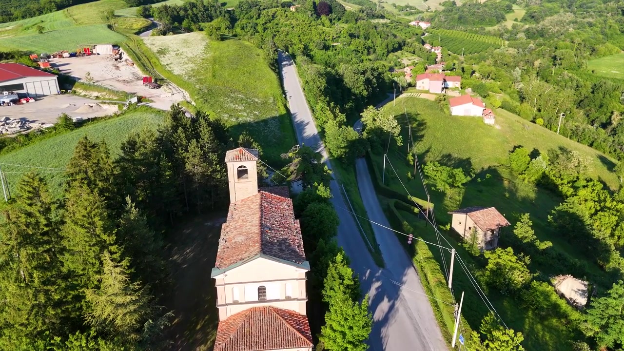 Riprese con drone mostrano una chiesa in pietra e una strada tortuosa attraverso le rigogliose colline verdi del Piemonte.