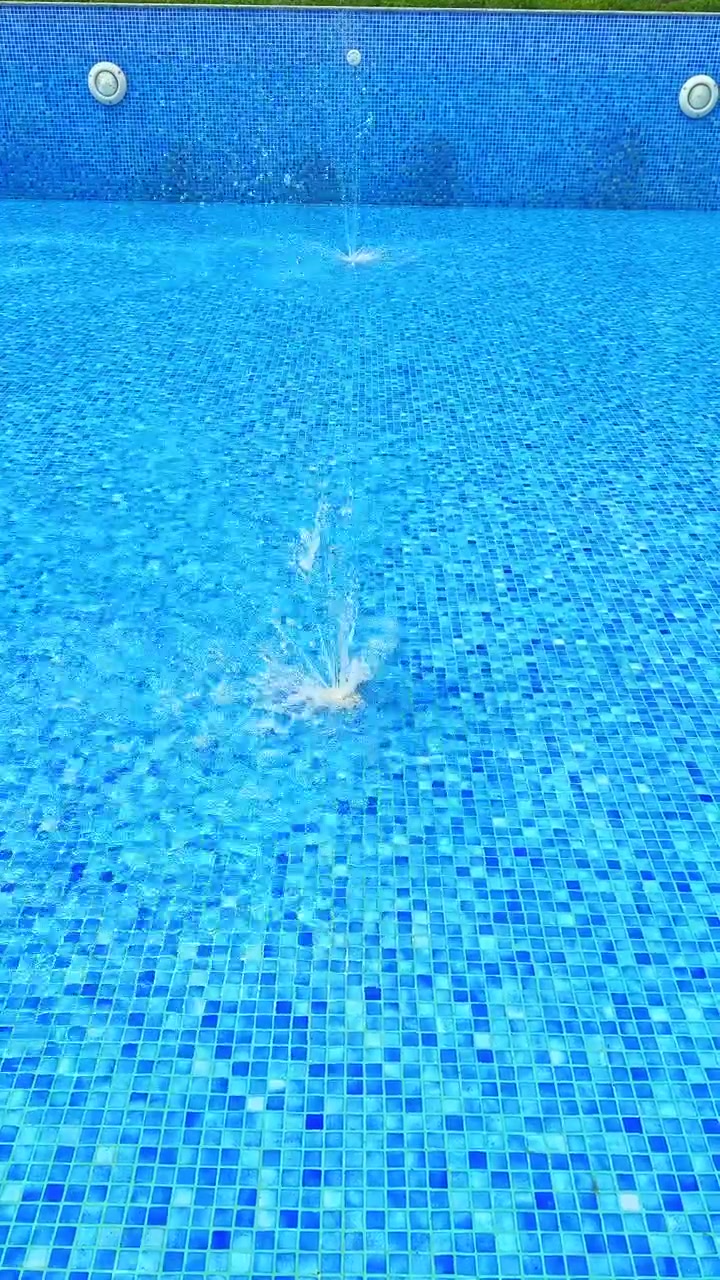 Air memercik di kolam berubin biru dengan fitur air mancur pada hari yang cerah