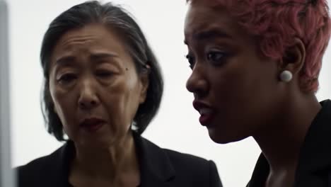 two women engage in a serious conversation in a well-lit workspace. one woman appears concerned while the other seems to explain something important related to their project.