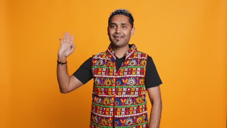 Portrait-of-jolly-man-smiling-and-waving-hand,-saluting,-studio-background