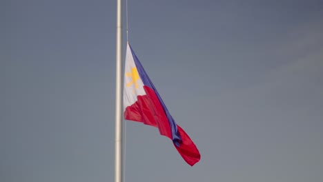 gran bandera filipina en un mástil gigante, con pájaros volando más allá en cámara lenta