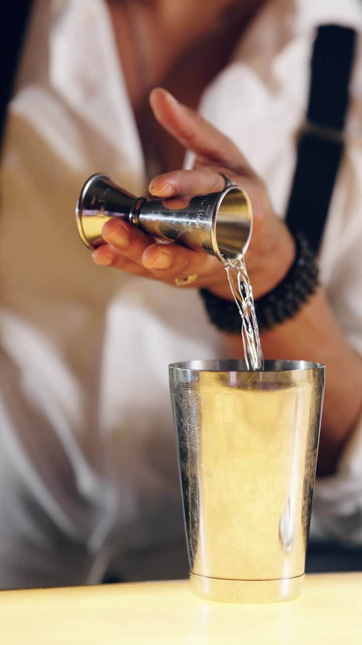 Barman che versa liquido da un jigger in uno shaker per cocktail.