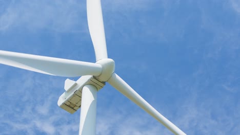 looking up to a big white wind turbine spinning isolated on blue sky with clouds