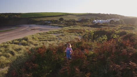 drone shot of young girl on beach vacation playing in sand dunes with evening light