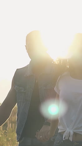 exciting close view young couple lit by back sunlight walks on field under orange sky in summer evening slow motion